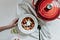A female hand reaches for a bowl of chilli sitting on a white dishcloth. A red Le Crueset pan sits nearby