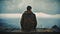 man in hooded jacket sitting on stone wall looking out over landscape and stormy sky