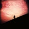 Photo of the dark silhouette of a person walking in front of a pink sunset.