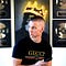 Picture of Kevin David standing in front of a big wall poster and his awards