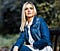 girl with long blonde hair wearing long sleeve blue denim jacket and white shirt with foliage background