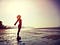 Silhouette of woman standing, arms oustretched, on a beach at sunrise
