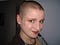 A young woman with a shaved head smiles cheekily at the camera