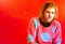 Ariel Pink looking sad in a pink sweater with blue polka dots and a blazing red background.