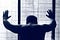 A man with his back to the camera and his hands on a patterned window, seemingly in frustration or depression