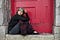A respectable looking middle-aged woman sits in a doorway with a blanket over her knees