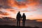Couple facing sunset with backs turned to the camera and holding hands.
