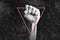 A clenched fist raised against a grey background, with a pink triangle in outline around it, as if hanging off the knuckles