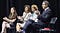 2015 panel with Governor Cuomo, Nancy Pelosi, Lt. Gov. Kathy Hochul, and presumably an aide to the governor’s office on a stage with folding chairs and black curtain