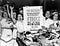 Women store clerks raise their fists and raise a sit-down strike sign demanding a 40-hour work week for Woolworth workers.