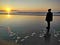 A woman on the beach watches the setting sun on the water.
