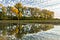 A cloudy blue sky and trees with yellow leaves are reflected in calm waters.