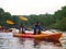 Two women wearing life vests kayak on a river.