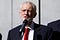 Photo of Jeremy Corbyn wearing a red tie with his black suit jacket and white shirt on while speaking into a mic