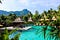 A beautiful, relaxing hotel scene in a lush jungle. Bungalows sit over turquoise water with mountain peaks in the distance.