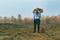 A photo of a man with an elephant face standing in a field with a briefcase next to him.