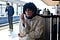 Curly haired woman in a sweater sitting at a train station smoking a cigarette and staring into the camera