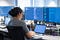 Back vision of a woman sitting on a desk looking at a computer and two monitors while programming.