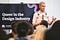 John presenting slides to audience wearing a pale pink oxford underneath a holographic leather bulldog harness.
