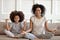 A mother and daughter sat on a couch in lotus pose, meditating and smiling.