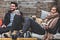 A smiling couple drink hot drinks and enjoy each other’s company with a cute dog on her lap.