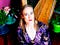 Composer Hannah Lash in purple floral shirt sitting in front of a harp and assorted potted plants