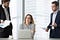 A businesswoman smiles awkwardly and looks away as two of her colleagues are bothering her with questions at her desk.
