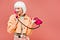 young woman in white-blonde wig wearing an orange jacket talking on a hot pink corded phone on dusty rose background