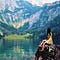 girl with long dark hair wearing yellow dress sitting on boulder looking out over lake and mountains