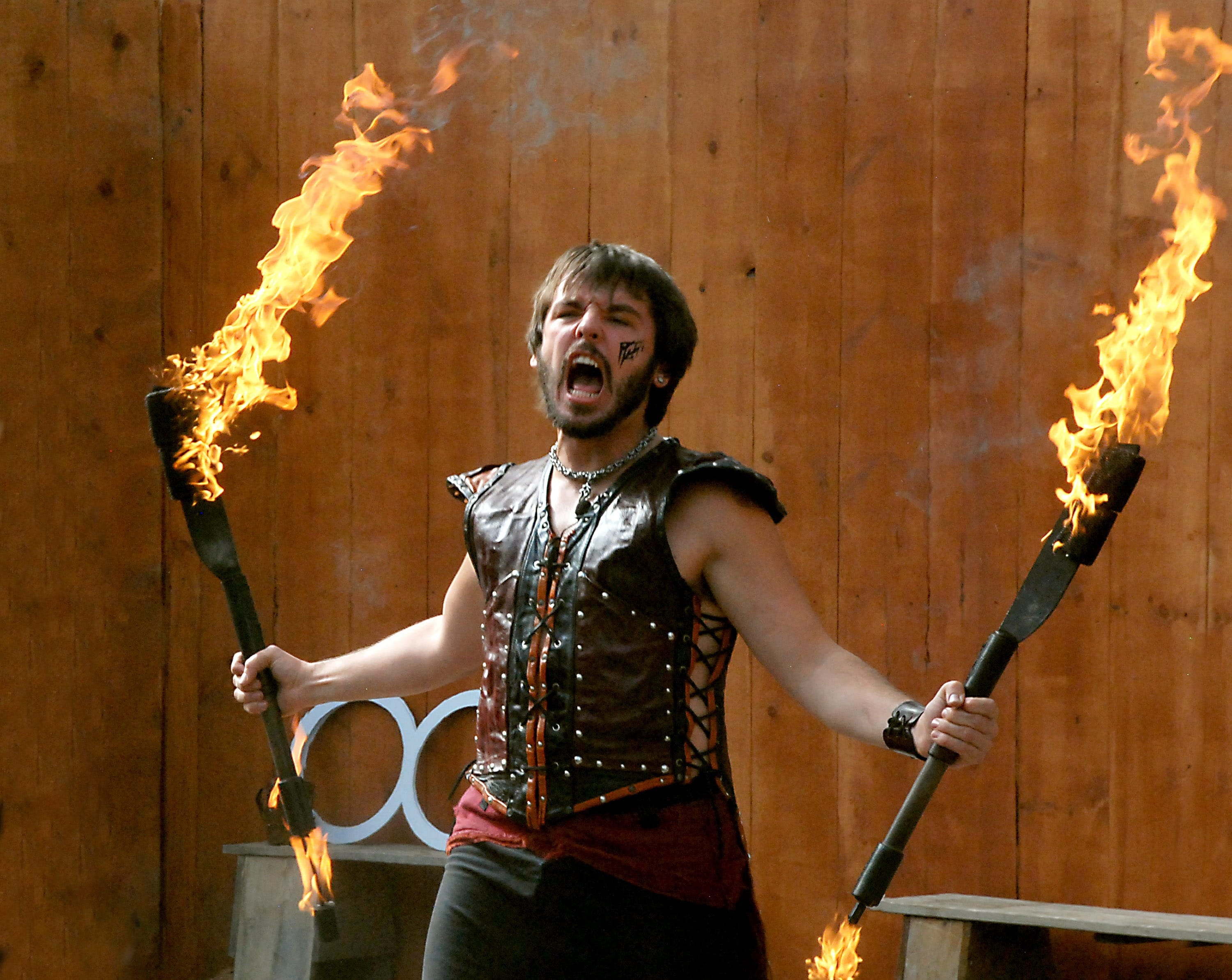 Angry young man in a medieval-looking tight-fitting vest holding two burning torches and yelling