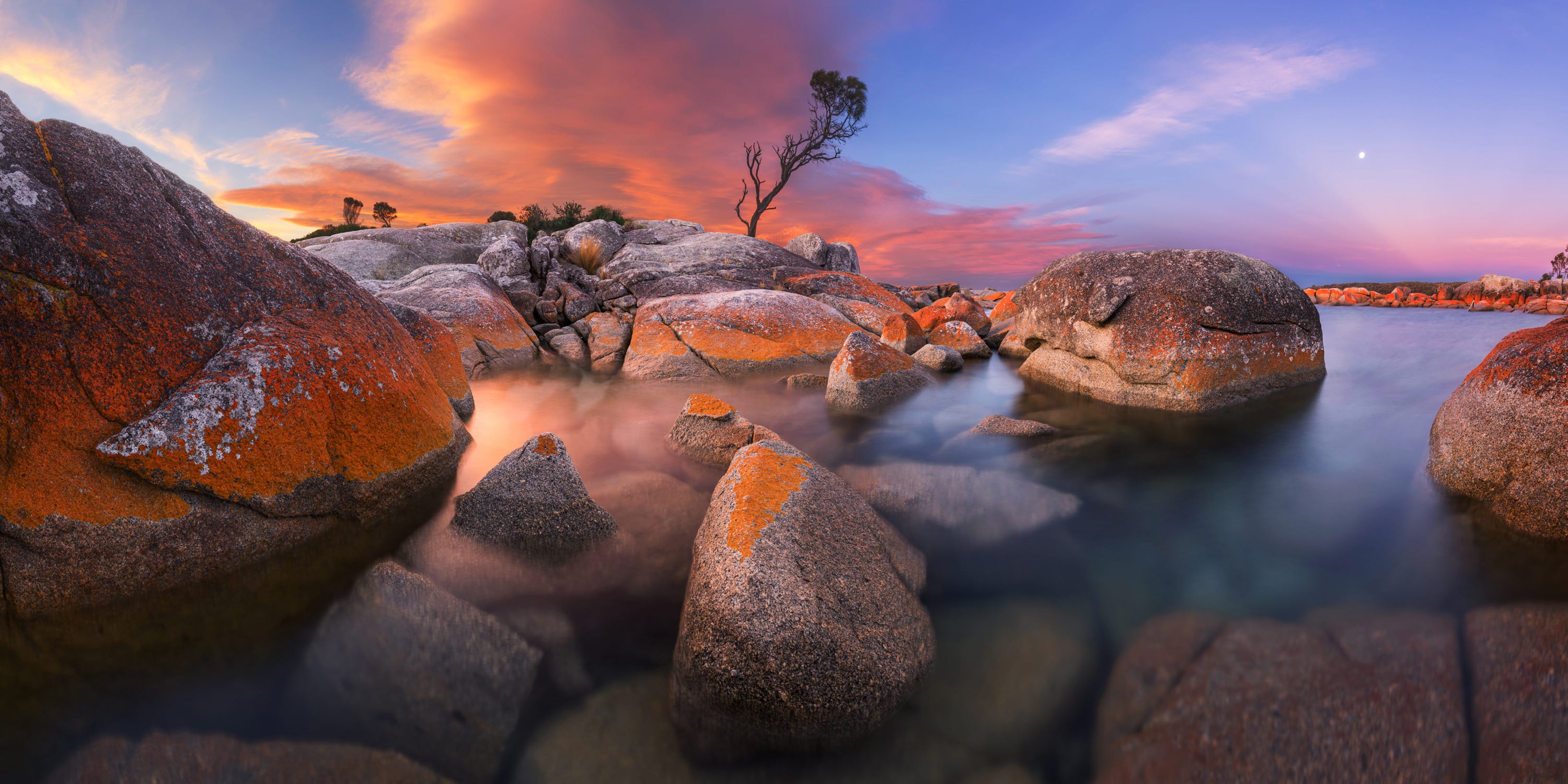 A sunset bathes rocks and water in orange and lavender light