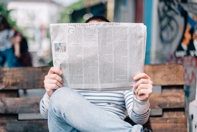 Man sitting on bench reading newspaper