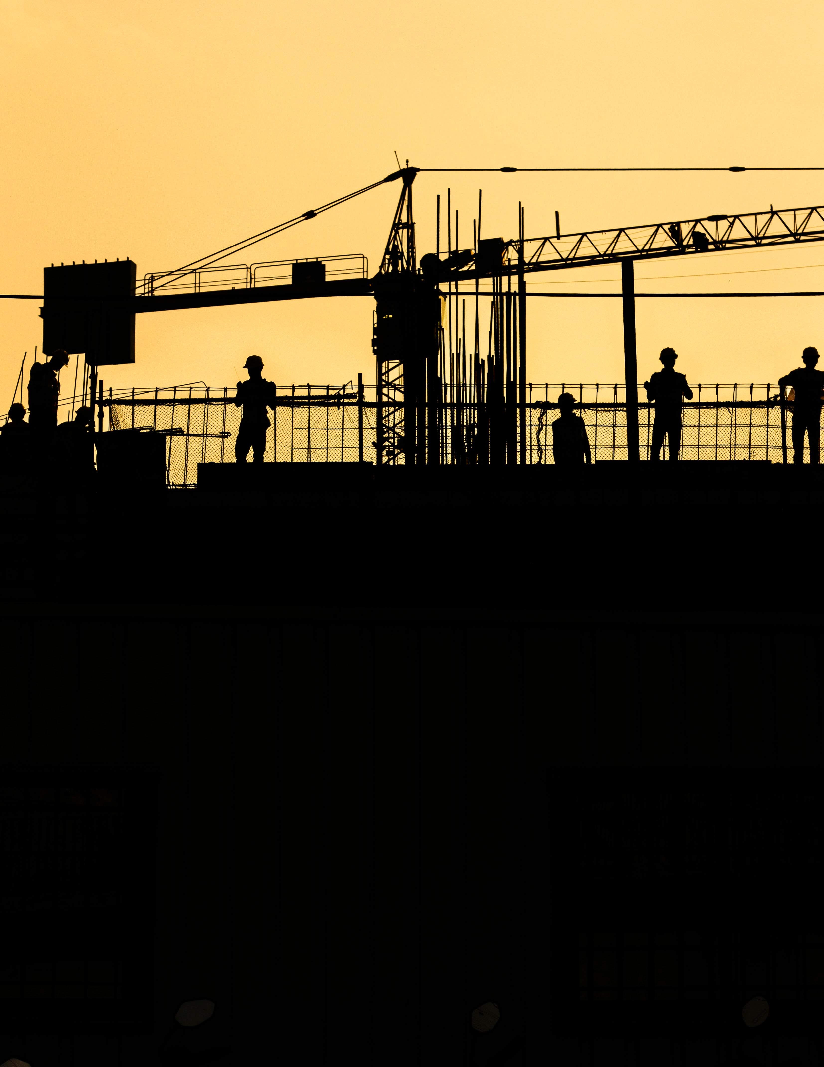 Sihouette of people standing at a construction site with a crane in the background.