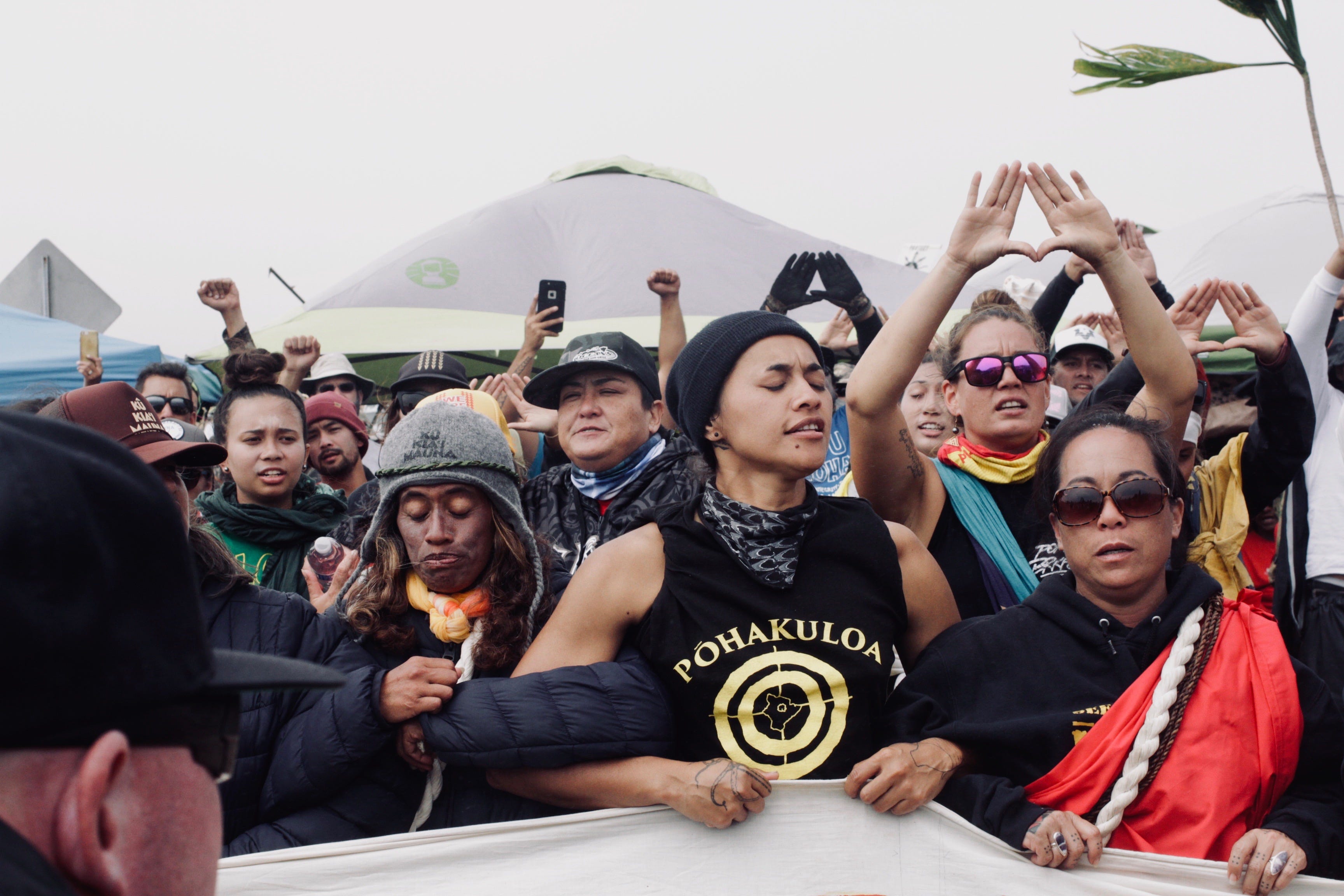 A photo of womxn and nonbinary folx creating a human barrier between the police and the kūpuna.