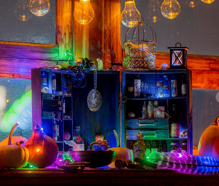 A colorful display of apothecary materials in a large wooden display case. Pumpkins surround the display.