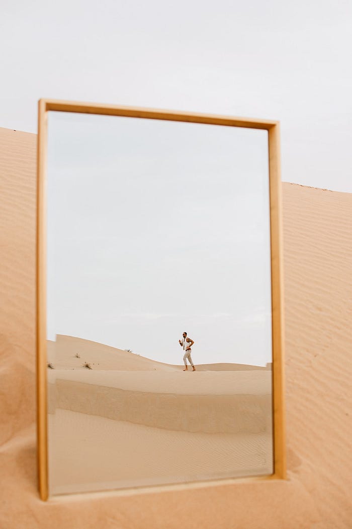A mirror showing the reflection of a man running across sand dunes in the desert.
