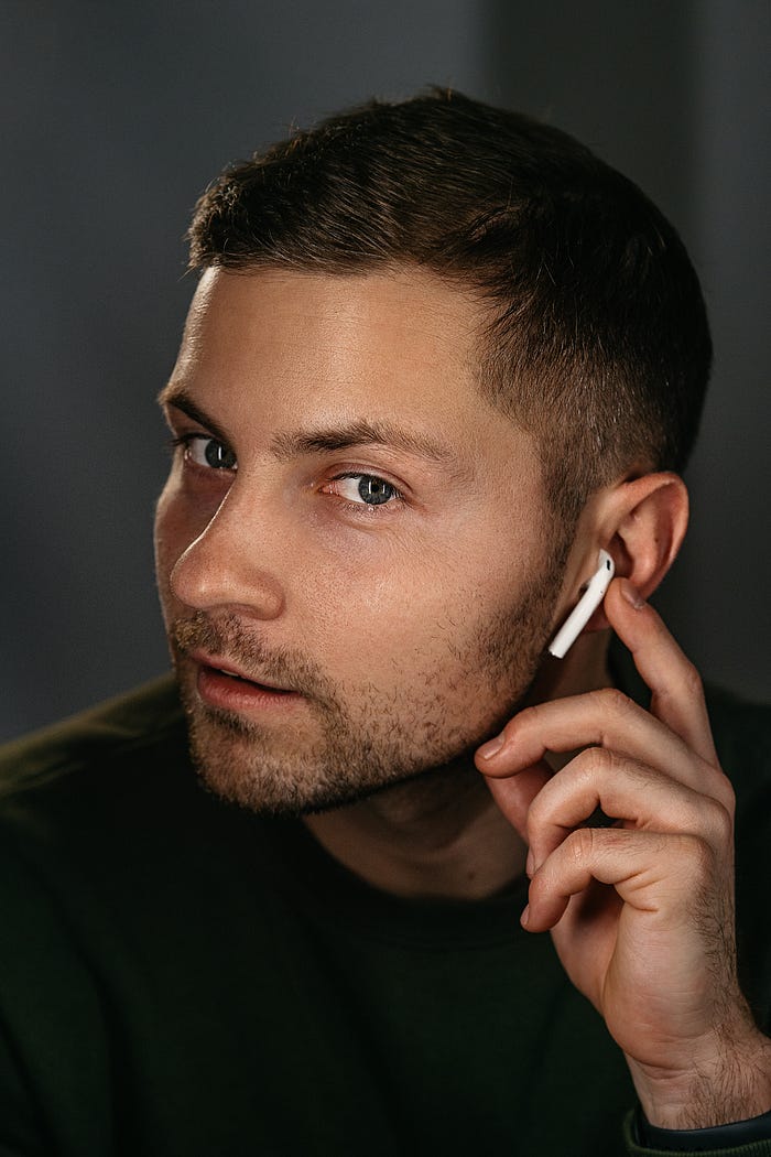 A portrait of a man with Apple Airpods in his ears, touching one of them with his finger.