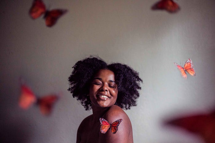 A woman with a beautiful smile. She has black hair. And in the background images of orange coloured butterflies