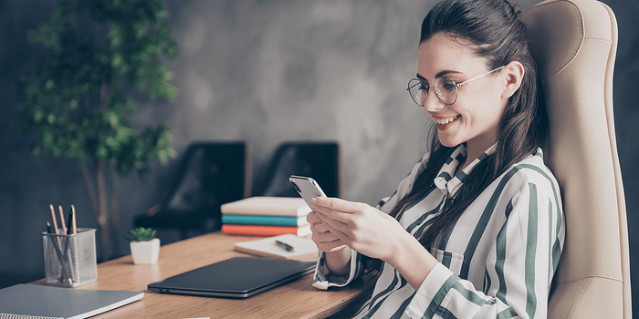 A woman sitting in an office with her phone in hands.