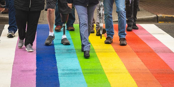 A group of people walking through a rainbow crosswalk.