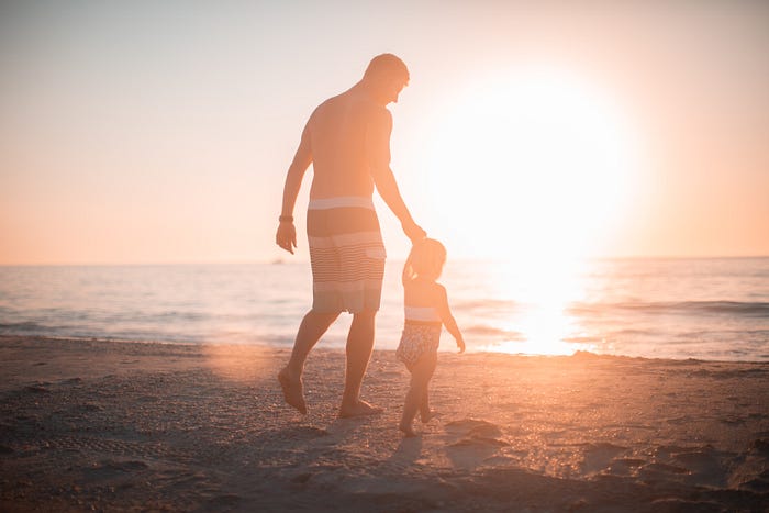 A photo of a dad and young daughter on a beach at sunrise.