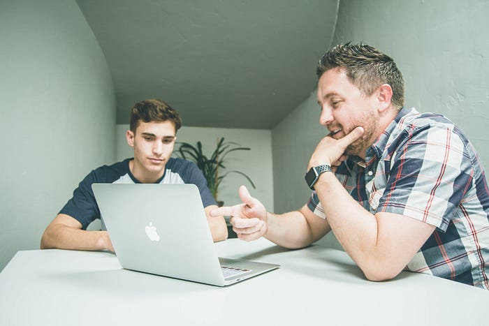 Two people talking in front of a macbook