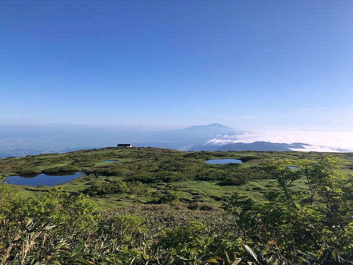 Mt. Chokai stands proud in the blue sky in the background with The Eighth Station of Mt. Gassan of the Dewa Sanzan and the Midagahara Marshlands in the foreground.