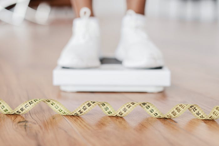 Woman standing on digital scale, body mass index, measuring tape