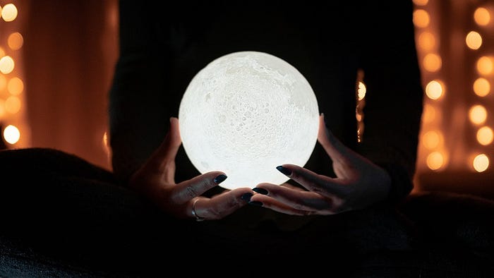 How To Really Debunk Astrology Using The Barnum Statement / Barnum Effect — A person holding a crystal ball that is lit and resembles the moon