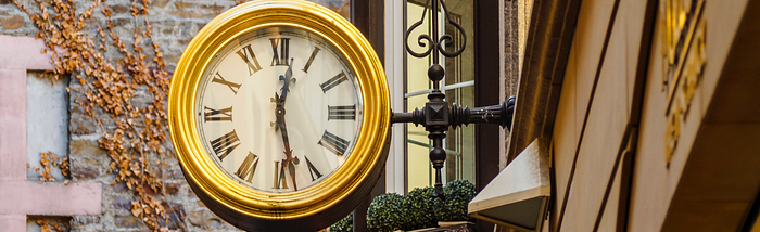 An old clock with Roman numerals, attached to the outside of a shop.