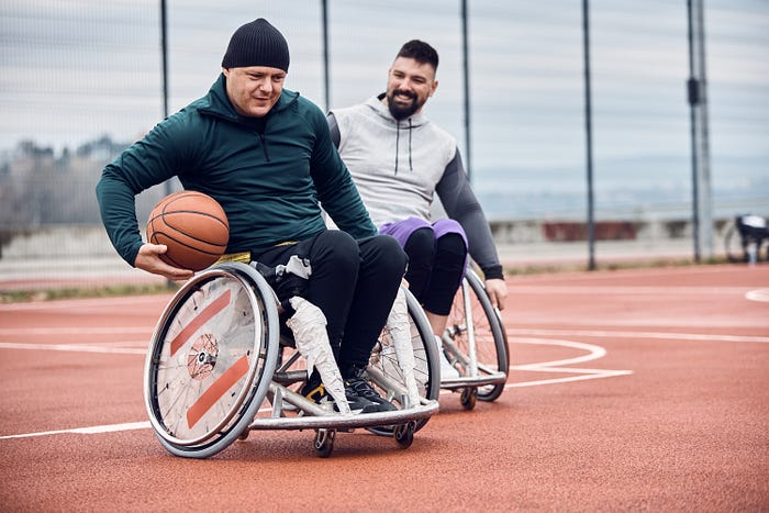 Body diversity includes people of different abilities, this photo shows two men engaged in wheelchair basketball and having fun. Everyone is happy, showing size inclusivity of people of all sizes, content relevant to body mass index (BMI), level of fitness, health, wellness, exercise, nutrition, healthy living, healthy lifestyle, weight stigma, anti-fat phobia, new norm, healthy weight