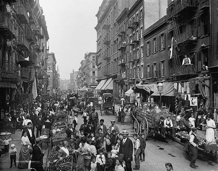Black and white photo of vendors and people crowded in the street in NYC in 1900