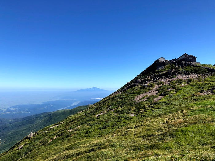 Mt. Gassan shrine of the Dewa Sanzan stands tall over the Shonai Plains and Mt. Chokai in the blue sky in the distance