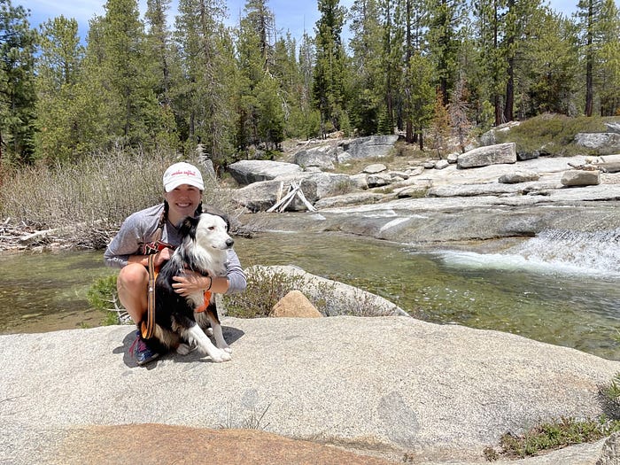 Amy holding her dog that looks like a border collie mix at a river